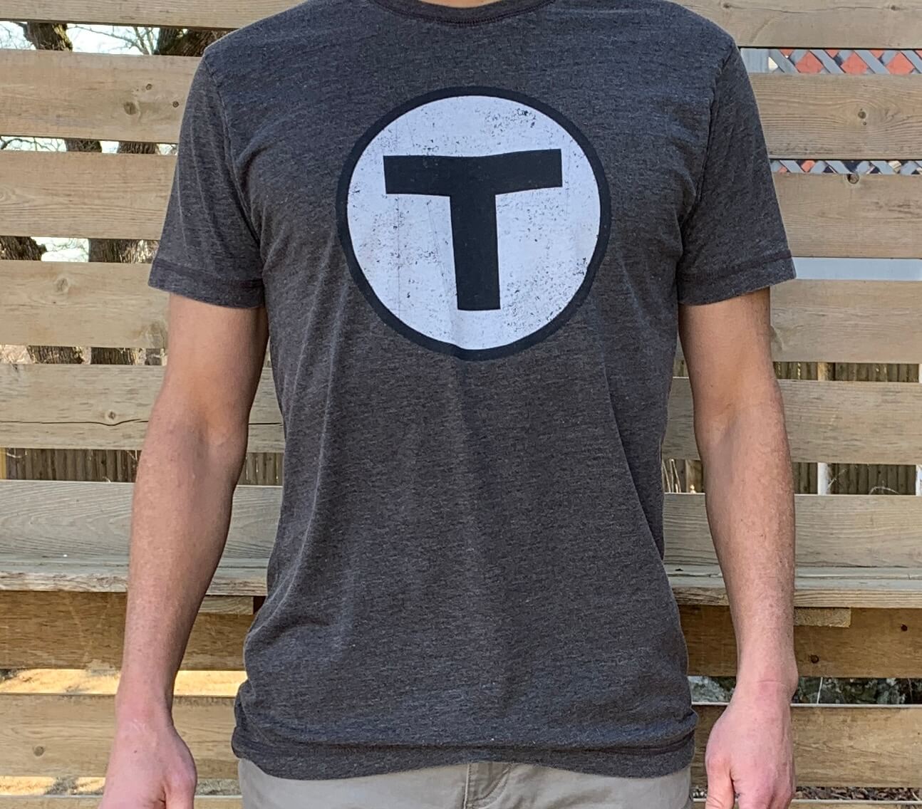 Man wearing faded black heavyweight t-shirt with black and white Boston MBTA T logo in the center chest
